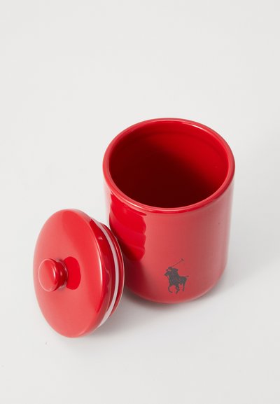 Sarkans keramisks trauks ar apaļu vāku un gludu virsmu, ar mazu pogu augšpusē un melnu jātnieka logotipu sānos.