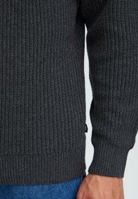 Mörkgrå stickad tröja med ribbat mönster, med långa ärmar och en figursydd nederkant, ihop med blå denimjeans.