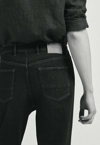 Svarta denimjeans med en figurnära design, med bakfickor och en ljusgrå märkeslapp i midjan. Tyget har en jämn textur.