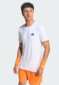 T-shirt de sport blanc à rayures verticales, logo Adidas noir, associé à un short orange et des bracelets assortis. Texture lisse, manches courtes.