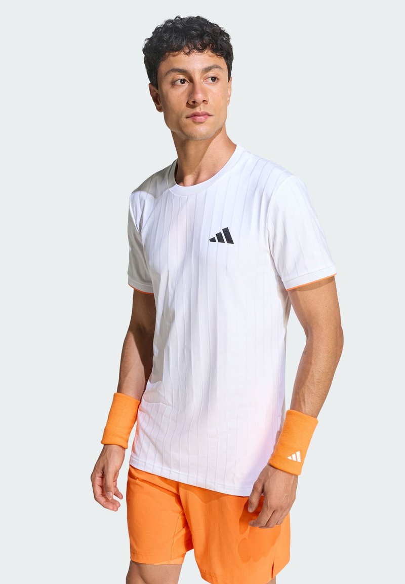 T-shirt de sport blanc à rayures verticales, logo Adidas noir, associé à un short orange et des bracelets assortis. Texture lisse, manches courtes.