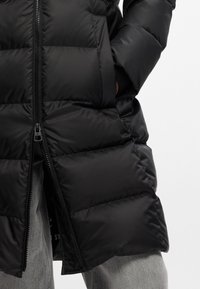Giacca a vento nera con finitura testurizzata, con zip completa, tasche laterali e design fino al ginocchio.