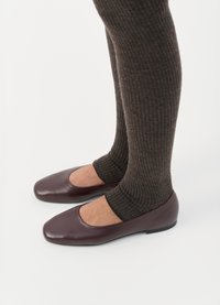Ballerine in pelle laccata bordeaux con design a punta quadrata, abbinate a calze in maglia a costine marrone scuro che arrivano a metà polpaccio.