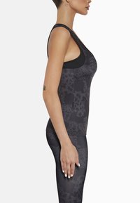 Czarny sportowy top na ramiączkach z teksturowanym wzorem, z okrągłym dekoltem i szerokimi ramiączkami, zestawiony z ciemnymi legginsami.