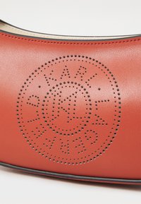 Red leather bag featuring perforated circular logo design and black accent edging. Smooth texture with a semi-gloss finish.