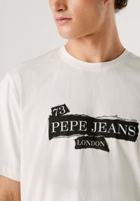 Biele bavlnené tričko s krátkymi rukávmi a okrúhlym výstrihom. Na prednej strane je čierna grafická potlač s textom "73 PEPE JEANS LONDON" v štýlovom usporiadaní.