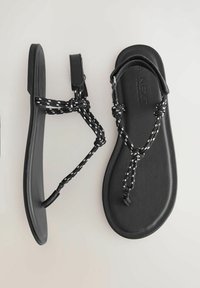 Black flat sandals with textured rubber soles and braided black and white straps. Buckle closure on the ankle strap.