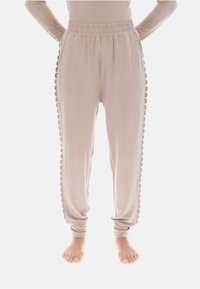Beżowe spodnie dresowe z elastycznym paskiem w talii i falistym zdobieniem po bokach; miękki materiał z zwężanymi nogawkami, bez kieszeni.