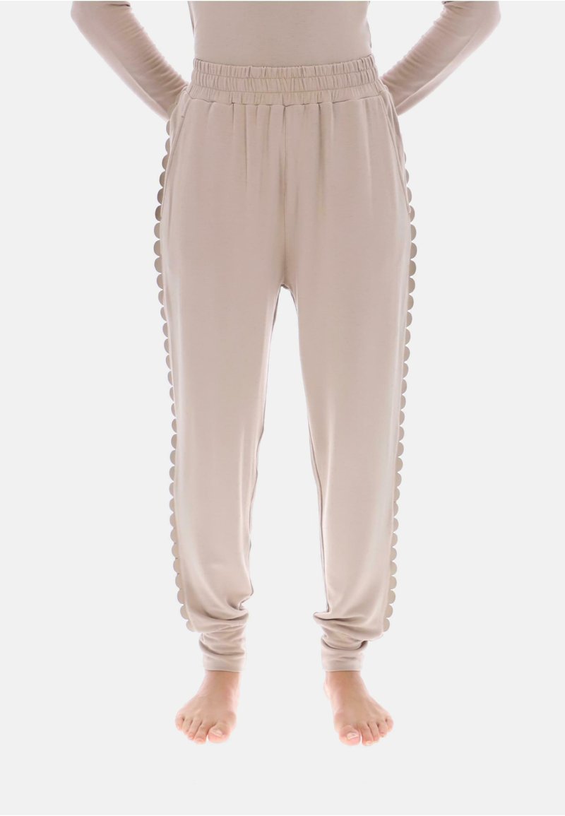 Beżowe spodnie dresowe z elastycznym paskiem w talii i falistym zdobieniem po bokach; miękki materiał z zwężanymi nogawkami, bez kieszeni.