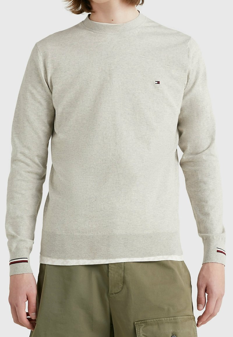 Hellgrauer Pullover mit langen Ärmeln, rundem Ausschnitt, gerippten Bündchen und Saum, mit einem kleinen Logo-Detail auf der Brust. Weiche Textur.
