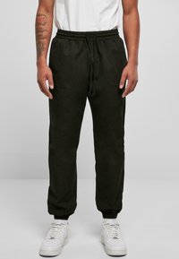 Mörkgröna, lätta joggers med elastisk midja och mudd, utrustade med sidofickor och en avslappnad passform, tillsammans med vita sneakers.