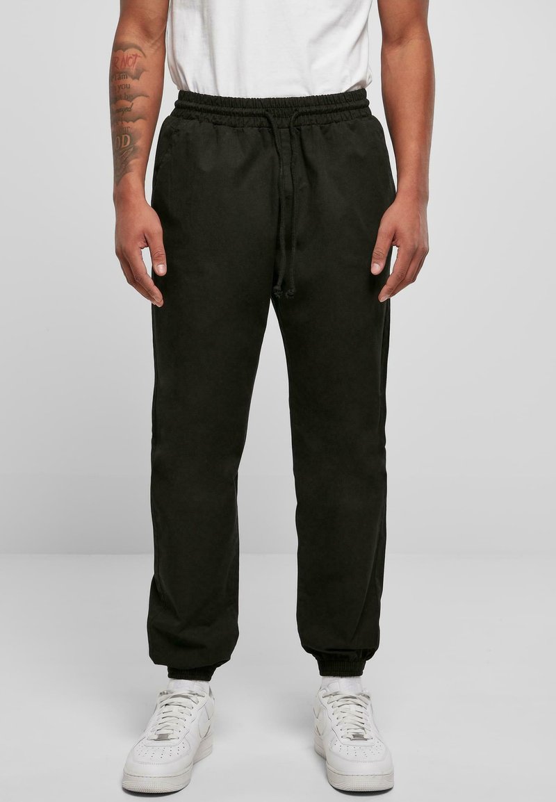 Mörkgröna, lätta joggers med elastisk midja och mudd, utrustade med sidofickor och en avslappnad passform, tillsammans med vita sneakers.