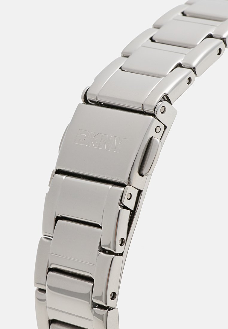 Bracciale in acciaio inox argentato con design a maglie, caratterizzato da superfici lucide e un logo DKNY inciso sulla chiusura.