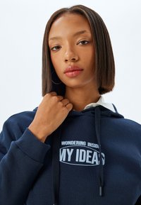 Sudadera azul marino con textura de algodón, con un diseño de texto gráfico que dice "PENSANDO EN MIS IDEAS" en blanco, y cordones ajustables.