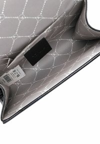 Svart läderplånbok med ett grått fodrat inre som har ett geometriskt mönster, en fack för etikett och en synlig produktetikett.