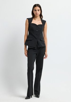 Completo nero su misura con blusa strutturata senza maniche e scollatura quadrata, bottoni sul davanti e pantaloni aderenti.