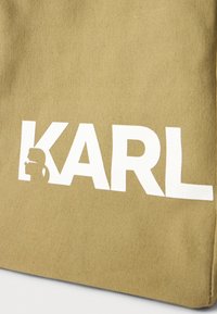 Sac de cană în verde măslin cu text alb îndrăzneț "KARL" și un logo în siluetă. Material texturat fabricat dintr-un material durabil.