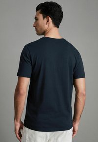 Tricou din bumbac negru, cu guler rotund și mâneci scurte, având o textură fină și o croială regulată, văzut din spate.