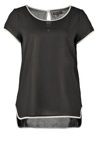 Blouse noire à manches courtes avec un liseré blanc sur les manches, le col et l'ourlet, dotée d'une petite fermeture à bouton au dos et d'un tissu légèrement transparent.