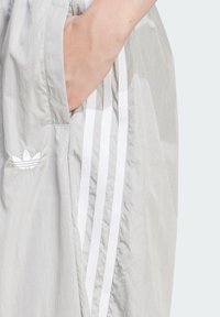 Ljusgrå sportshorts med en textur, med tre vertikala vita ränder och en broderad vit logotyp på fickan.