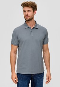 Polo shirt gris en tissu texturé et côtelé ; avec un col classique, une patte de boutonnage à trois boutons et des manches courtes. Coupe décontractée, associé à un jean bleu.