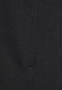 Felpa nera con una texture morbida, dotata di tasca a marsupio e dettagli di cucitura sottili. Il materiale sembra leggero e confortevole.