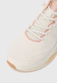 Lightweight athletic sneaker in cream with pink accents, featuring a textured mesh upper, thick laces, and a gum rubber outsole.