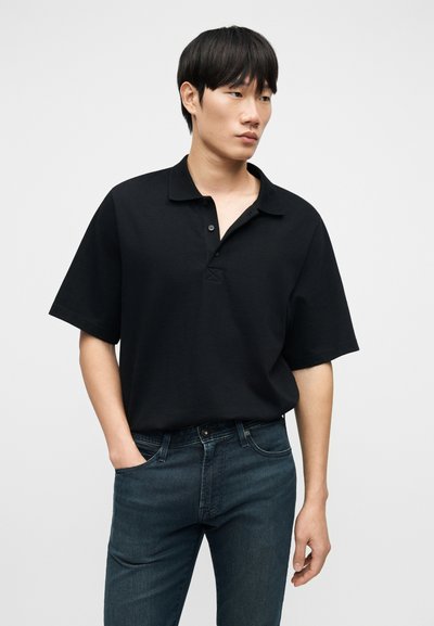 Μαύρο κοντομάνικο πόλο μπλουζάκι με γιακά με κουμπιά, κατασκευασμένο από απαλό βαμβάκι. Συνδυάζεται με σκούρα μπλε τζιν με κλασική εφαρμογή.