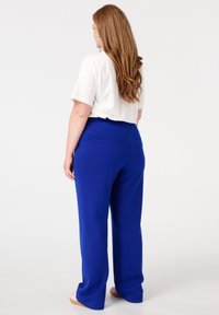 Blauwe wijde broek van een gladde, rekbare stof met een comfortabele elastische tailleband en achterzakken. Gestyled met een wit T-shirt met korte mouwen.