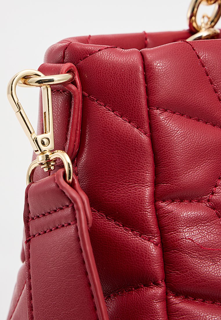 Sac à main en cuir matelassé rouge avec quincaillerie dorée, une forme structurée et une bandoulière amovible avec un détail de fermoir.