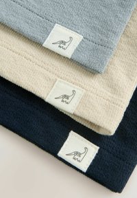 Trois tissus en gris, beige et marine, présentant un tissu texturé et de petites étiquettes avec un motif de dinosaure cousues sur le côté.