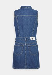 Dżinsowa sukienka bez rękawów z kołnierzykiem, dopasowanym wcięciem w talii i rozkloszowaną spódnicą. Niebieski kolor z dwiema kieszeniami z tyłu i metką z logo przy talii.