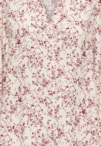 Hvit bluse med knapper foran, prydet med små burgunderrøde blomster jevnt fordelt over stoffet, og med V-utringing.