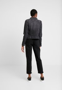 Czarna kurtka dżinsowa o krótkim kroju, z kołnierzykiem i widocznymi przeszyciami. Połączona z czarnymi spodniami i sportowymi butami.