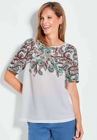 Lichte, luchtige witte blouse met ingewikkelde paisleystiksel in teal, oranje, en bruin op de mouwen en aan de voorkant. Ronde hals en korte mouwen.