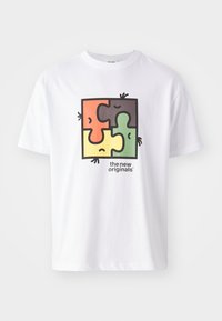 Weißes T-Shirt mit einem quadratischen Puzzle-Grafik in Rot, Grün, Gelb und Schwarz. Der Text lautet "die neuen Originals". Aus weichem Baumwollmaterial.
