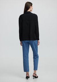 Maglietta nera a maniche lunghe con una texture sottile, tessuto leggero e dettaglio sul retro, abbinata a jeans blu a gamba dritta e tacchi neri.
