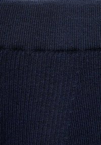 Temno modra pletenina z rebrasto teksturo. Material prikazuje fine navpične črte in ima mehak, nekoliko puhast videz.