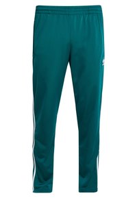 Türkise Jogginghose mit elastischem Bund, Seitentaschen und weißen Seitenstreifen. Glatte Textur, schmaler Schnitt und Markenlogo in Hüfthöhe.