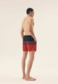 Spodenki kąpielowe z granatową górą i czerwonym dołem, zdobione pionowymi paskami. Wykonane z lekkiego materiału, przeznaczone do codziennego noszenia.