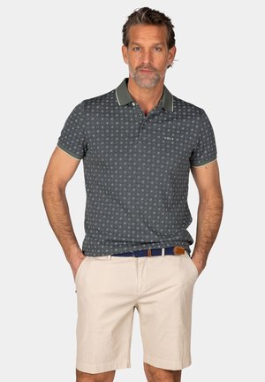 Marine poloshirt met een subtiel cirkelpatroon, contrasterende kraag en mouwboorden, gecombineerd met beige shorts en een blauwe riem.