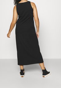 Schwarzes Baumwoll-Maxikleid mit ärmellosem Design, runder Ausschnitt und fließender Silhouette, kombiniert mit schwarzen High-Top-Sneakern.