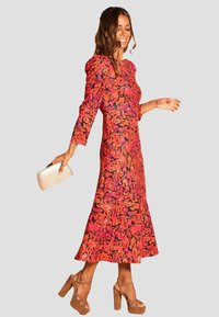 Abito attillato a maniche lunghe con un motivo astratto arancione e rosa, fondo svasato e tessuto testurizzato. Abbinato a una pochette dorata e tacchi beige.