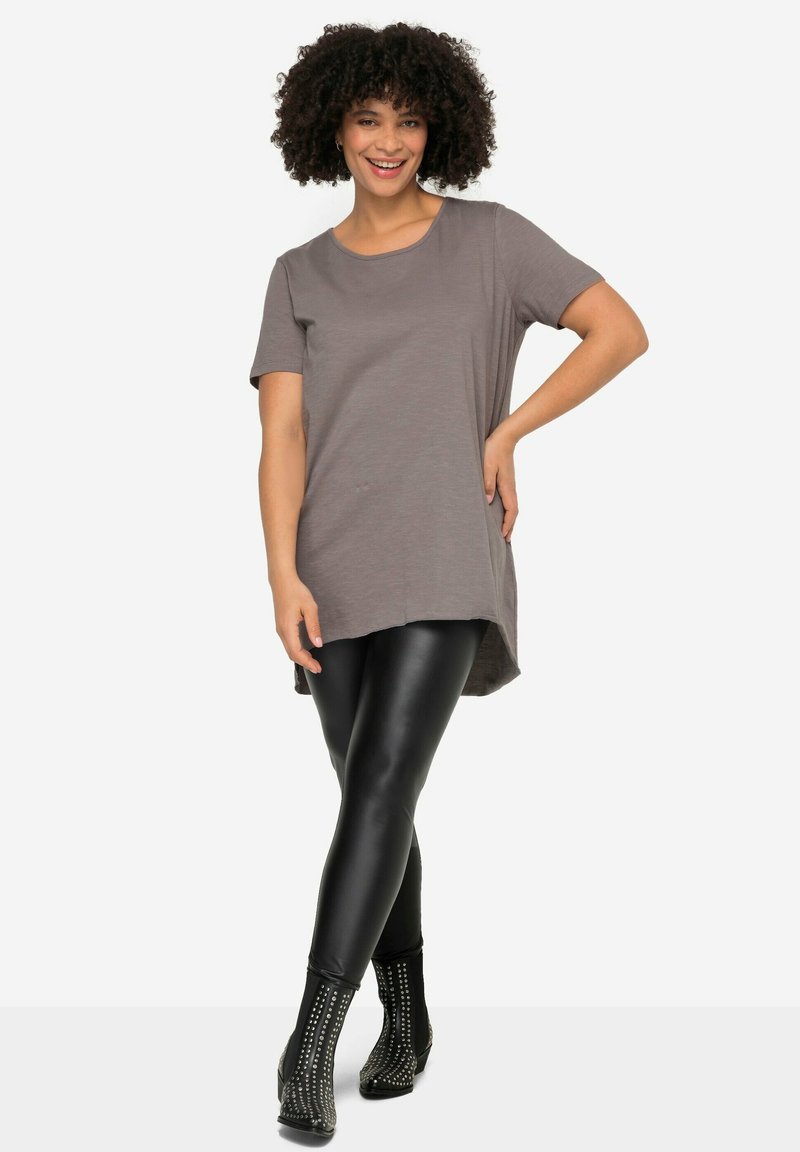Graues, kurzärmliges Tunika-Oberteil mit rundem Halsausschnitt, kombiniert mit schwarzen, figurbetonten Leggings und genoppten Ankle-Boots.