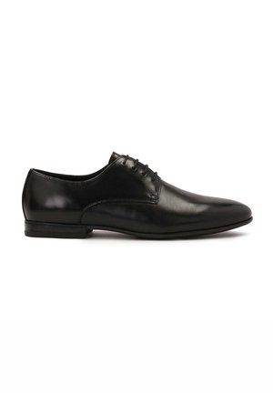 Zapato oxford de cuero negro con una textura suave, puntera puntiaguda y cinco ojales para los cordones. Presenta un tacón bajo y un diseño minimalista.