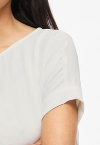 Blusa bianca a maniche corte con una texture morbida e leggera. Presenta un collo a barca semplice e maniche arrotolate.