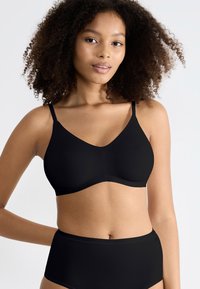 Brassière noire avec des bretelles réglables, texture lisse et décolleté en V. Associée à une culotte noire taille haute assortie.