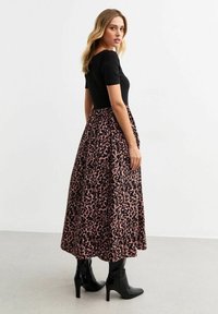 Black fitted top with short sleeves paired with a long, flowy pink leopard-print skirt, complemented by glossy black high-heeled boots.