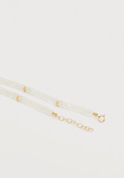 Λευκό κολιέ με χάντρες με χρυσά διαχωριστικά και χρυσή αλυσίδα με επέκταση και κούμπωμα τύπου ελατηρίου σε λευκό φόντο.