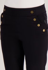 Zwarte stretchbroek met een aansluitend ontwerp, voorzien van gouden knopen op de tailleband en zijzakken voor extra detail.